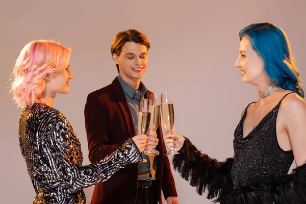 Sonrientes y elegantes amigos queer tintinear copas de champán durante la fiesta de Navidad sobre fondo gris - foto de stock