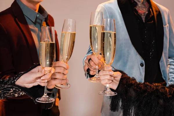 Cropped view of people in elegant clothes holding champagne glasses on grey background — Stock Photo