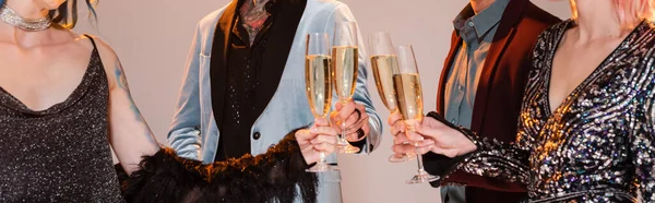 Partial view of stylish nonbinary friends clinking champagne glasses on grey background, banner — Stock Photo