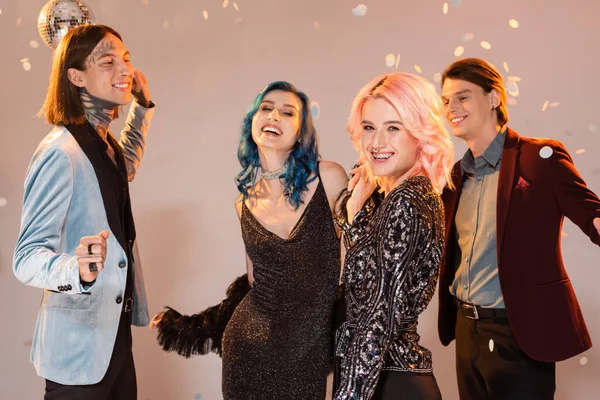 Cheerful queer person looking at camera while dancing with nonbinary friends on beige background — Stock Photo