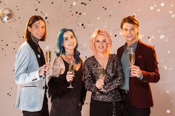 Pessoas não binárias alegres com copos de champanhe olhando para a câmera enquanto celebra o Natal no fundo bege — Fotografia de Stock