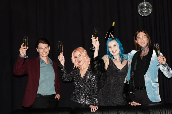 Happy and stylish queer people toasting with champagne while celebrating christmas and looking at camera on black background — Stock Photo