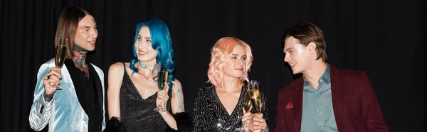 Elegant and happy queer people holding champagne glasses and talking on black background, banner — Stock Photo