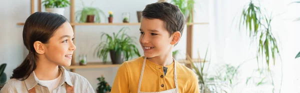 Lächelnde Kinder, die einander in der Nähe verschwommener Pflanzen zu Hause anschauen, Banner — Stockfoto