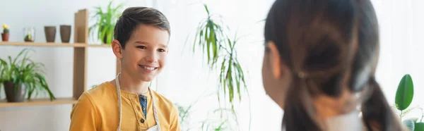 Preteen boy looking at blurred friend near plants at home, banner — Stock Photo