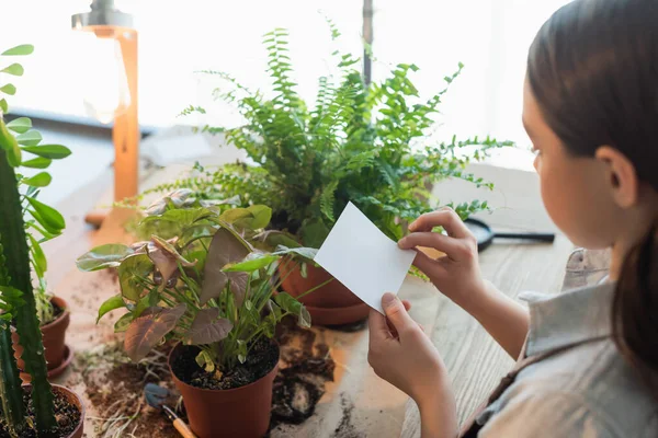 Child holding sticky note near plants and soil on table at home — Stock Photo