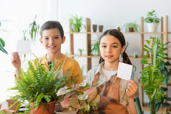 Preteen kids holding sticky notes near plants at home — Stock Photo