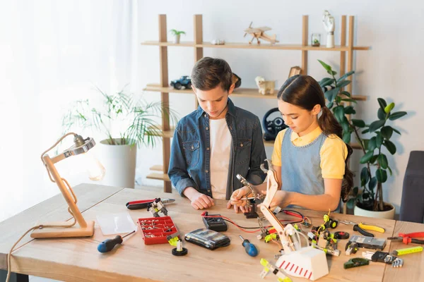 Preteen kids making robotic model near lamp at home — Stock Photo