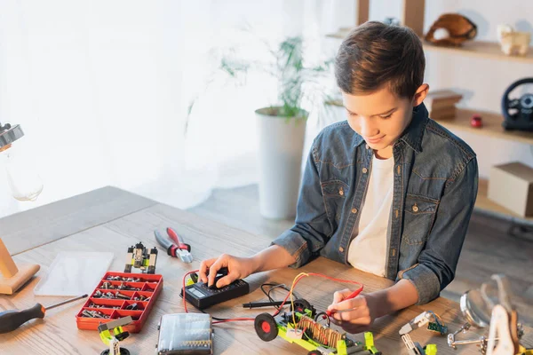 Menino pré-adolescente fazendo modelo robótico com milímetros perto de ferramentas e parafusos em casa — Fotografia de Stock