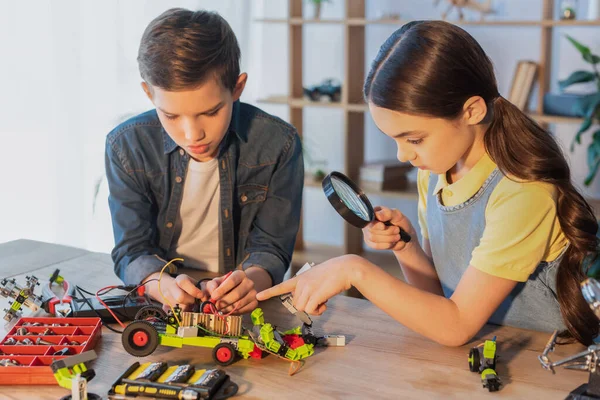 Fille avec loupe pointant avec doigt ami proche faisant modèle robotique — Photo de stock