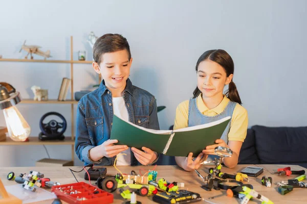 Lächelnde Kinder mit Notizbuch in der Nähe von Robotermodell und Werkzeug zu Hause — Stockfoto