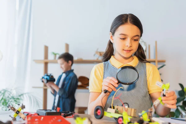 Kid holding magnifying glass and robotic model on table at home — Stock Photo