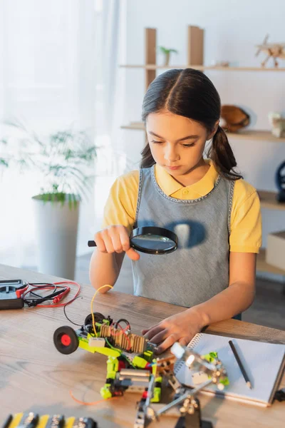 Preteen child looking at robotic model through magnifying glass at home — Stock Photo