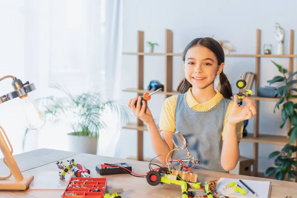 Smiling preteen girl looking at camera while holding screwdriver and robotic model at home — Stock Photo