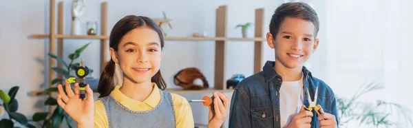 Enfants heureux avec des outils et une pièce mécanique souriant à la caméra à la maison, bannière — Photo de stock