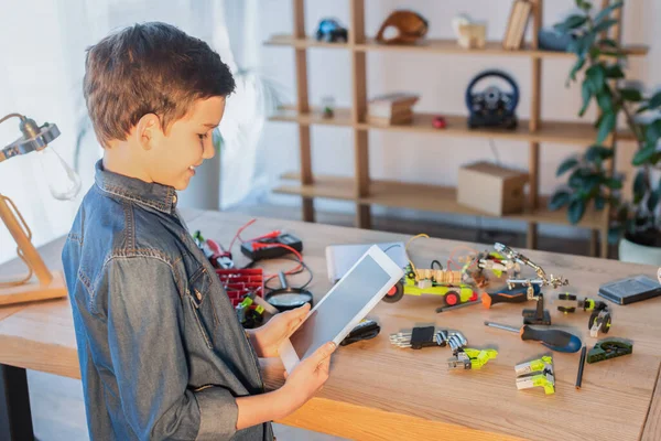 Ragazzo preadolescente sorridente con tablet digitale vicino agli strumenti e dettagli del modello di robotica sul tavolo — Foto stock