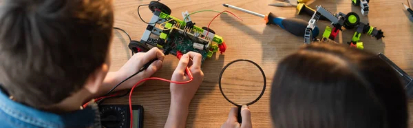 Vue de dessus du garçon mesurant la tension du modèle robotique près de la fille avec loupe, bannière — Photo de stock