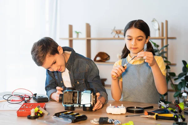 Preteen girl holding screwdriver while boy assembling car model near mechanical parts on table — Stock Photo