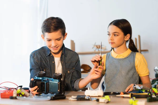 Preteen girl holding screwdriver near friend looking at handmade car model at home — Stock Photo