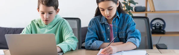 Chica escribiendo en el cuaderno cerca de amigo usando el ordenador portátil en casa, bandera - foto de stock