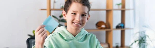 Cheerful boy showing empty sticky note and smiling at camera, banner — Stock Photo