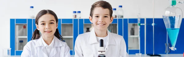 Glücklich preteen Freunde Blick auf Kamera in der Nähe Kolben mit Flüssigkeit im Labor, Banner — Stockfoto