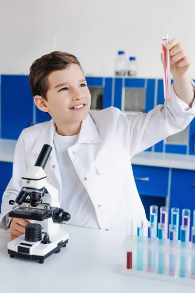 Ragazzo felice guardando la provetta vicino al microscopio in laboratorio chimico — Foto stock