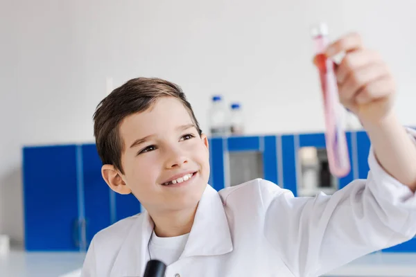 Fröhlicher Preteen-Junge schaut auf verschwommenes Reagenzglas, während er chemische Experimente im Labor macht — Stockfoto