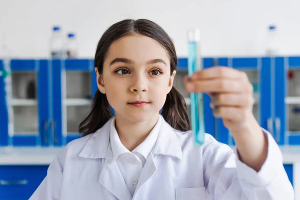 Brünettes Mädchen im weißen Mantel hält verschwommenes Reagenzglas im Labor — Stockfoto