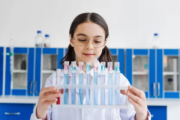 Smiling preteen girl in eyeglasses holding test tubes in laboratory — Stock Photo