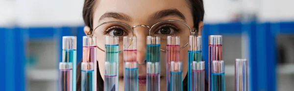Preteen girl in eyeglasses looking at camera near test tubes in lab, banner — Stock Photo