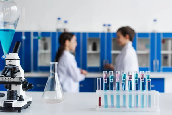 Selective focus of test tubes and microscope near children on blurred background in chemical lab — Stock Photo