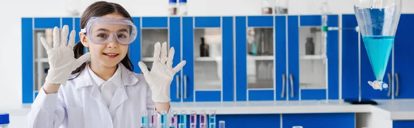 Chica sonriente mostrando las manos en guantes de látex en laboratorio químico, pancarta - foto de stock