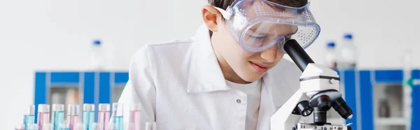 Kind in Schutzbrille schaut ins Mikroskop, während es chemische Experimente macht, Banner — Stockfoto