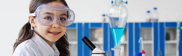 Feliz niña preadolescente en gafas mirando a la cámara en el laboratorio químico borroso, pancarta - foto de stock