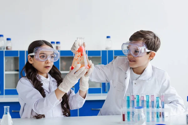 Glückliche Frühchen in weißen Mänteln, die in die Nähe von Mikroskop und Reagenzgläsern mit Fläschchen blicken — Stockfoto