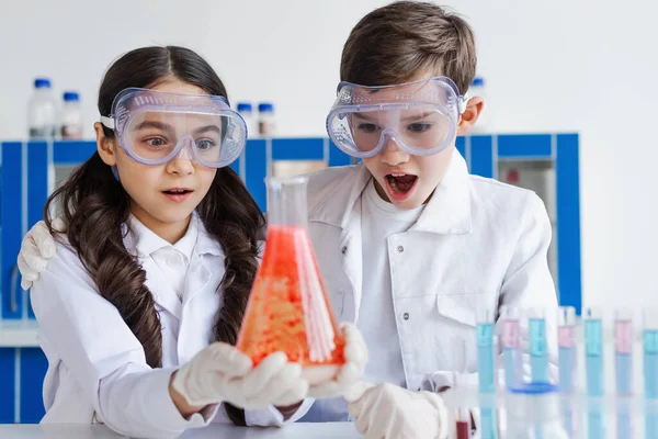 Amazed friends in goggles looking at flask with red substance in laboratory — Stock Photo
