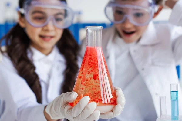 Selective focus of flask with red liquid with bubbles near amazed friends in blurred background — Stock Photo