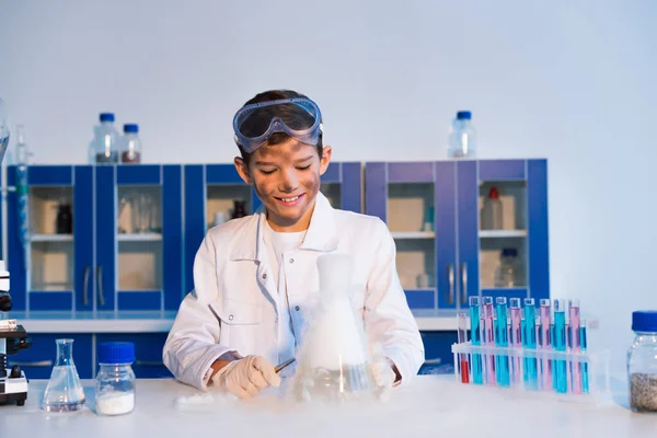 Souriant garçon avec sale visage regardant la substance fumante pendant l'expérience chimique — Photo de stock