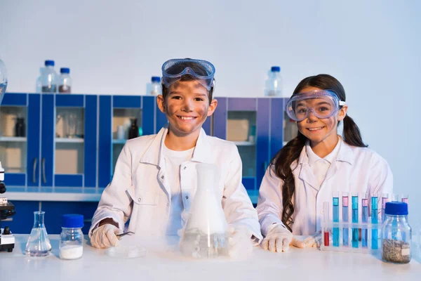 Щасливі діти з брудними обличчями, які дивляться на камеру під час хімічного експерименту в лабораторії — стокове фото