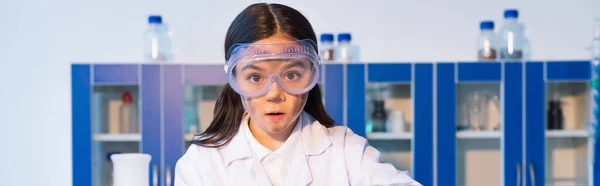 Surprised girl in goggles and with dirty face looking at camera in chemical lab, banner — Stock Photo
