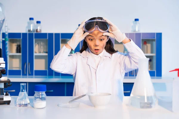 Scioccato ragazza con occhialini viso sporco e guardando ciotola durante l'esperimento chimico — Foto stock