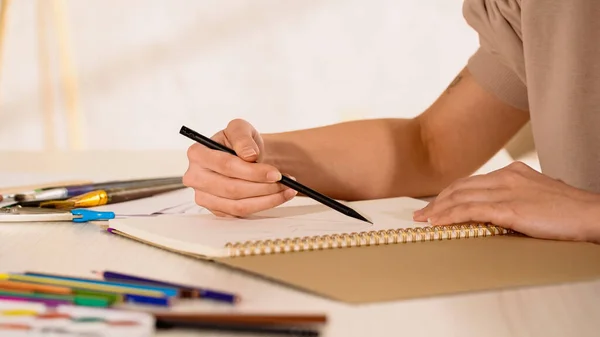 Vista recortada de la mujer dibujando en cuaderno de bocetos cerca de lápices de color borroso - foto de stock