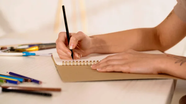 Vista ritagliata della donna tatuata che disegna su sketchbook — Foto stock