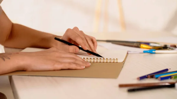 Vista recortada de la mujer con dibujo a lápiz en cuaderno de bocetos en casa - foto de stock