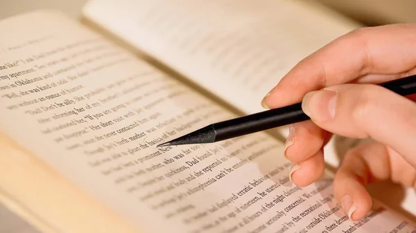 Vista da vicino della donna che tiene la matita vicino al libro a casa — Foto stock