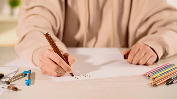 Ausgeschnittene Ansicht einer Frau, die auf Papier schreibt, in der Nähe von Zeichenkompass und Farbstiften zu Hause — Stockfoto