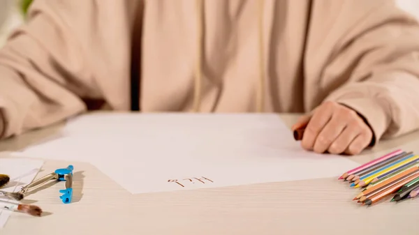 Обрезанный вид женщины, сидящей рядом с бумагой с высокой буквы и цветные карандаши дома — стоковое фото