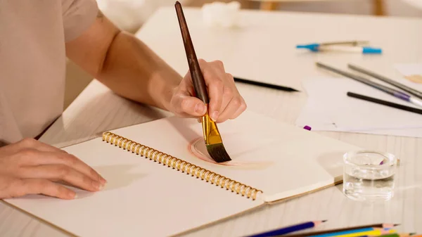 Vue partielle de la peinture de femme sur carnet de croquis près de l'eau sur la table — Photo de stock