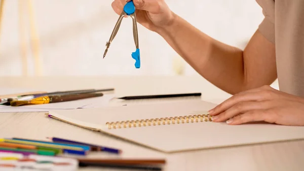 Vista recortada de la mujer sosteniendo brújula de dibujo cerca de cuaderno de bocetos en casa - foto de stock